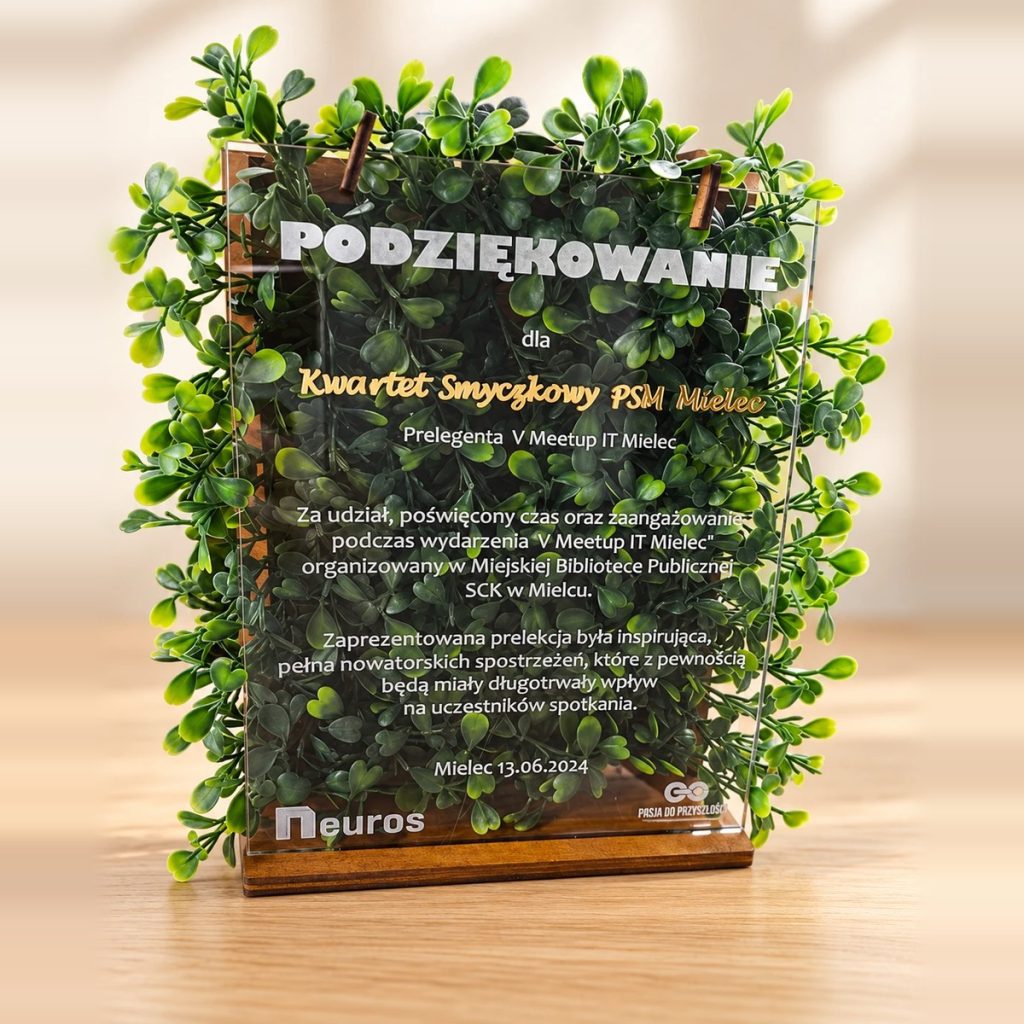 Akrylowa statuetka z podziękowaniem w drewnianej podstawie na tle zielonych listków, ze złotym napisem i tekstem