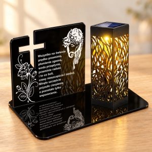 Czarna tabliczka pamięci z akrylu z wyciętym krzyżem, białym grawerem róży, wizerunku Jezusa i wiersza, obok czarny ażurowy lampion solarny LED